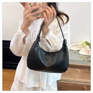 Detail view of black woven faux leather shoulder bag with zipper and slim handle strap