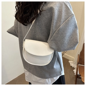 White semi-circular saddle bag made of smooth faux leather shown on shoulder for daily wear