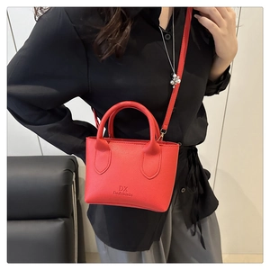Model wearing a red lychee leather bucket bag with top handles and adjustable strap