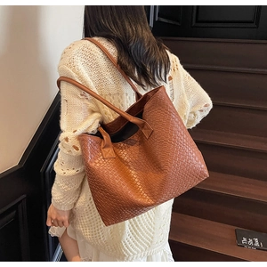 Grand sac cabas tressé marron porté par un mannequin sur un escalier en bois brun