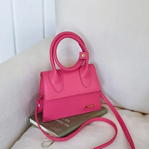 Petit sac à main magenta à poignée ronde et bandoulière posé sur un livre vert