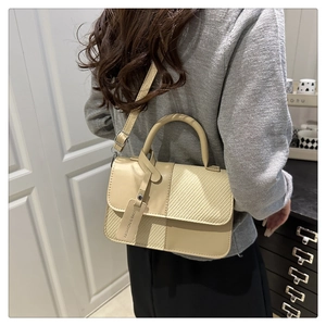 Détail du sac bandoulière beige montrant les coutures et la texture tressée avec boucles dorées