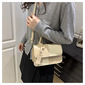 Détail d'un sac carré en cuir beige et tissage porté par un mannequin dans un intérieur