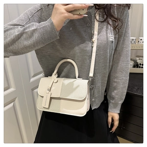 Gros plan du sac carré crème montrant la texture du cuir et la bandoulière réglable