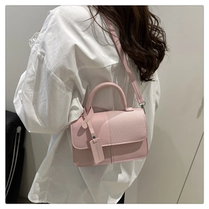 Sac à main rose avec texture tissée et étiquette, porté par un mannequin en extérieur
