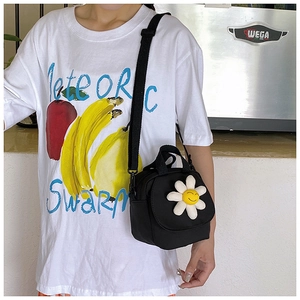 Detail of a black canvas crossbody bag with a white 3D daisy flower and smile embroidery