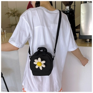 Detail of a black canvas crossbody bag with a white 3D daisy and yellow smiley face accent