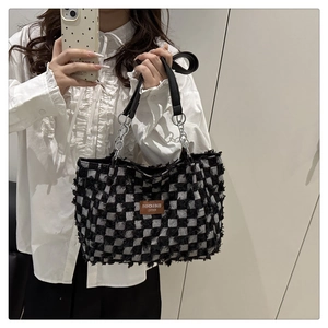 Close-up of black and white checkerboard tweed tote bag with metal chain strap worn by model
