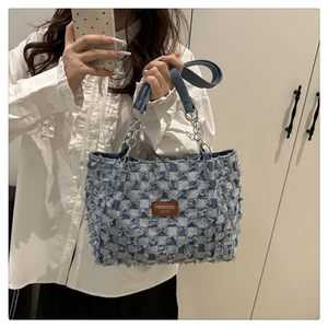 Detail of blue and white checkered denim tote bag with leather logo patch and metal chain