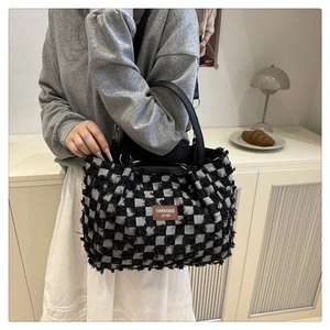 Close-up of black and white checkered tote bag with fringe details and leather patch
