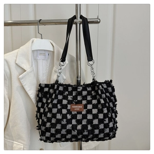 Detail of checkered tote bag with fringe edges and leather handles on display