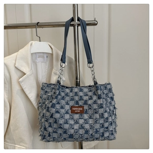 Detail of plaid denim shoulder bag with frayed edges and metal chain leather strap