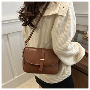 Brown leather saddle bag with gold buckle shown on shoulder in vintage interior