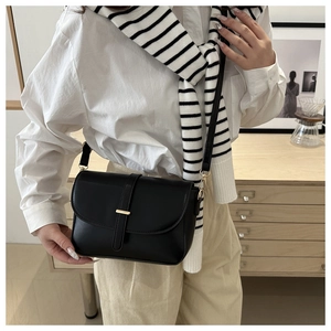 Detail view of a black leather crossbody bag featuring a golden metal bar and long strap
