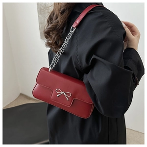 Détail du sac à bandoulière en cuir rouge avec boucle nœud argentée et bandoulière chaîne