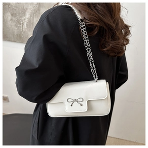 Rear view of model wearing a white bow flap bag with silver chain strap on black outfit