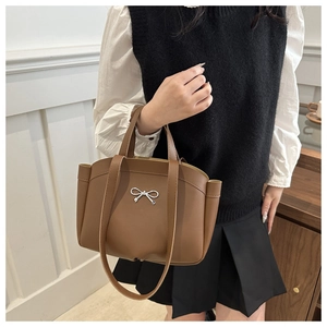 Detail of a large brown leather tote bag featuring a silver metal bow accent