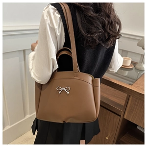Brown bucket bag with silver bow detail shown from a back view on a model