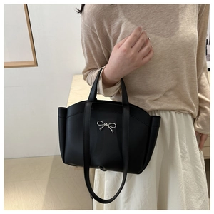 Detail of a black minimalist tote bag with a silver metal bow and adjustable strap