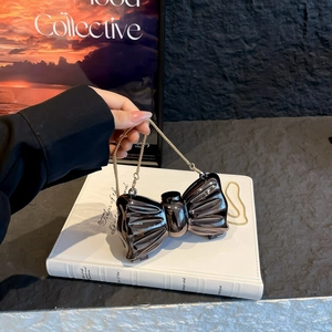 Mini metallic bow-shaped shoulder bag with gold chain strap on a white book surface