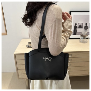 Close-up of minimalist black tote bag with silver bow detail and matte leather finish