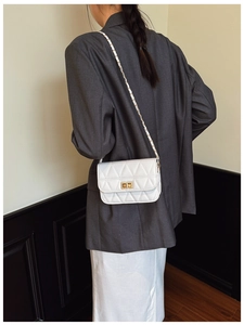 Close-up of white quilted crossbody bag with gold metal lock and leather chain strap