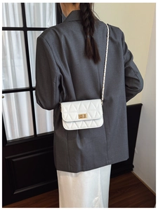Detail of white quilted crossbody bag with gold chain strap and metallic clasp on model