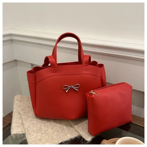 Red tote bag with silver bow buckle and matching pouch on elegant wooden surface
