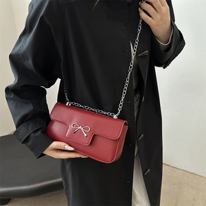 Elegant red flap crossbody bag with silver bow accent and delicate chain strap