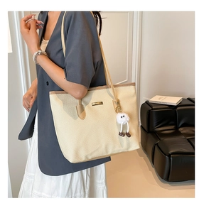 Dettaglio della borsa tote intrecciata beige con finiture in pelle e ciondolo a mostriciattolo