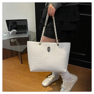 Close-up of white tote bag with embossed skull patterns and rhinestone metal buckle