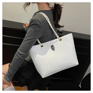 Detailed view of white tote bag featuring skull embossed pattern and metal chain strap