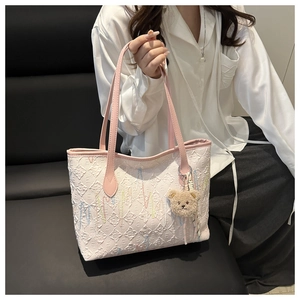 Detail of white quilted tote bag with pink straps and a plush bear charm on a model
