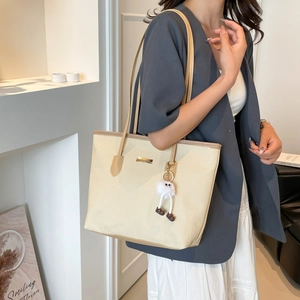 Large beige woven tote bag with brown leather trim and a cute plush charm accessory