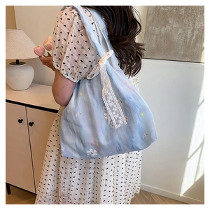 Detail of light blue floral fabric tote bag featuring a white lace bow shoulder strap