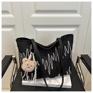 Detail of black tote bag with wavy embroidery and a plush bear charm on white books