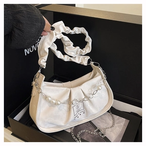 Détail d'un sac à main plissé blanc cassé avec perles et chaîne dans une boîte noire