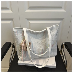 Detailed macro view of white quilted tote bag with wave embroidery and bear charm