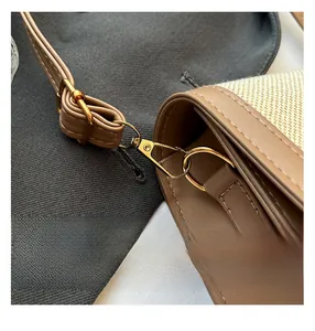 Close-up of the golden metal swivel hook and brown leather trim on a woven bucket bag