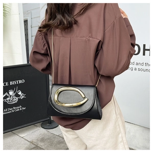 Detail of black leather crossbody bag with oversized gold buckle and chain strap