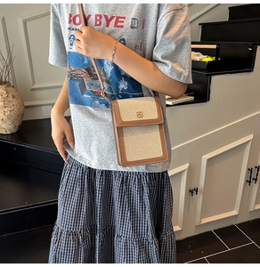 Détail d'un sac bandoulière en toile avec bordure cuir et fermoir trèfle sur modèle