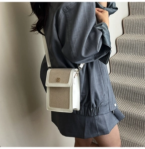 Crossbody bag detail with beige canvas, white leather, and clover metal logo on model