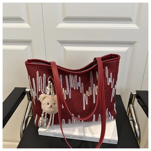 Close-up of wine red tote bag with colorful embroidery and a plush bear pendant
