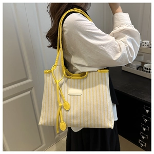 Detail of striped canvas tote bag with yellow leather trim and decorative tassel charm