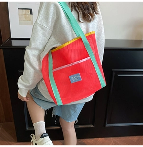 Detail of vibrant mesh tote bag with red body and contrasting green handles for beach travel