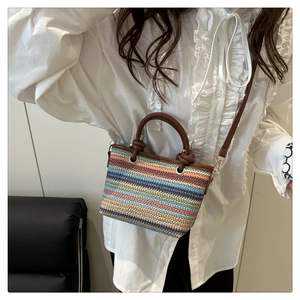 Crossbody shot of a colorful striped woven bucket bag with brown leather handles and strap