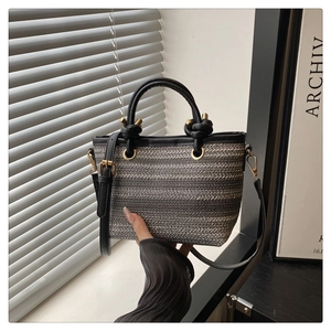 Detail of woven beach handbag featuring black leather knot handles and gold hardware