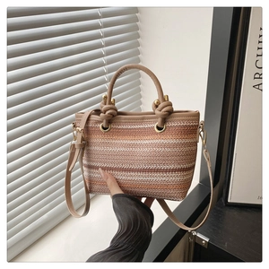 Detail of woven striped tote bag with leather handles and gold metal hardware accents