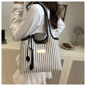 Detail of a large black and white striped canvas tote bag with leather straps and fringe