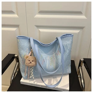 Detail of light blue tote bag featuring wave pattern embroidery and a cute brown bear charm